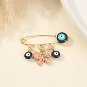 Gold-tone alloy safety pin brooch featuring blue evil eye beads and pink enamel butterfly charms.