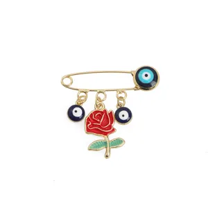 Gold tone safety pin brooch featuring red rose and blue evil eye charms, stylish detail.