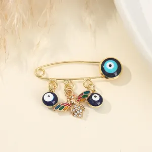 Gold tone safety pin brooch featuring evil eye beads and crystal bee detail detail shot.