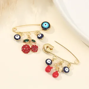 Gros plan détail de broche cerise en strass et mauvais œil, bijoux en métal doré.