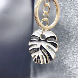 Close-up detail of stylish black and white enamel monstera leaf key ring alloy bag charm pendant.