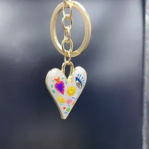 Gold alloy keychain featuring a white enamel heart pendant with colorful doodle art designs. Great accessory.