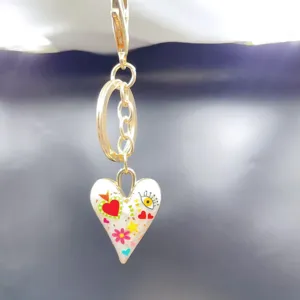 Gold alloy keychain with white enamel heart pendant and colorful doodle charms for bags.