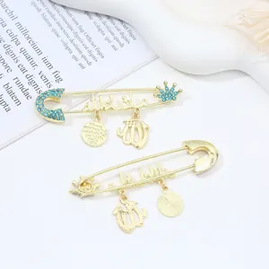 Gold safety pin brooch set with blue rhinestones, crown, and Arabic script charms.