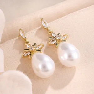 Close-up detail van elegante vergulde oorbellen met bloem zirkonia en parelhangers.
