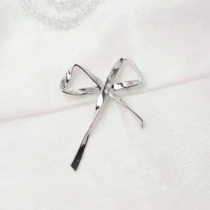 Dettaglio spilla fiocco asimmetrico in metallo argentato, elegante accessorio moda.