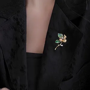 Detail shot of exquisite hibiscus flower brooch with dark pearl and green leaves on black fabric.