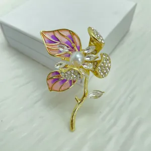 Elegant gold-plated floral brooch featuring vibrant enamel leaves, sparkling rhinestones, and a central pearl.