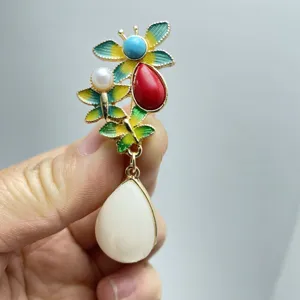 Close-up of vintage ethnic alloy brooch with colorful enamel, pearls, and teardrop pendant.