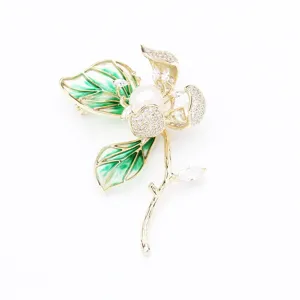Detailed view of exquisite gold-plated hibiscus flower brooch with green enamel and pearl.