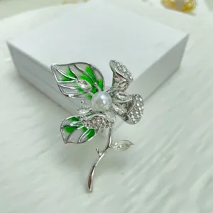 Closeup detail of silver flower brooch with green enamel, rhinestones and pearl.