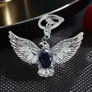 Close-up detail of metal eagle keychain with spread wings, black teardrop gem and cat-eye stones.