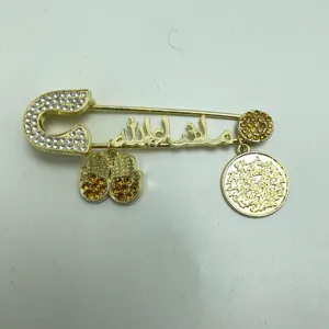 Close-up detail of a gold-toned rhinestone safety pin brooch with hamsa hand and coin charms.