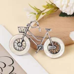 Close-up of vintage alloy bicycle brooch with imitation shell wheels and sparkling crystal accent.