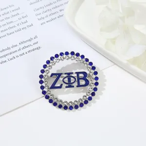 Close-up view of a circular rhinestone brooch with blue enamel Greek letters detail.