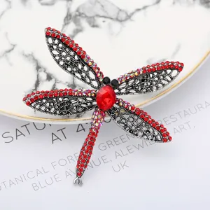 Detailed close-up of sparkling rhinestone dragonfly brooch with red crystals and silver wings.