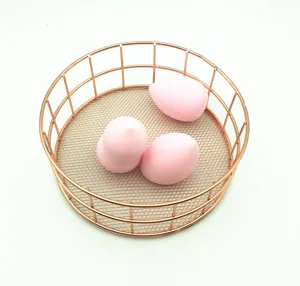 Detailaufnahme von rosa Make-up-Schwämmen in einem eleganten Roségold-Drahtkorb.
