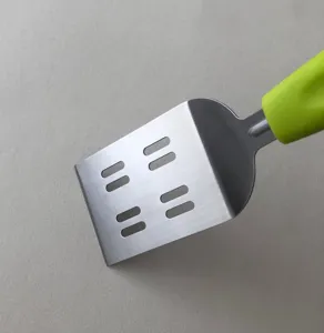 Stainless steel kitchen spatula detail, metal blade with slots and green handle.