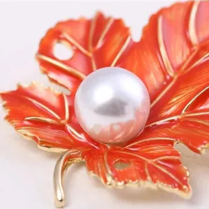 Macro detail shot of orange enamel maple leaf brooch featuring white pearl inlay and gold tone.