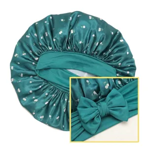 Green satin sleep bonnet with white cherry print and wide bow design for hair care.