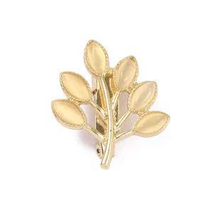 Detailaufnahme einer filigranen goldfarbenen Blatt-Brosche mit glatten, milchigen Steinen.