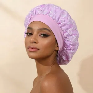 Close-up detail of purple satin hair bonnet with floral embroidery and wide elastic band.