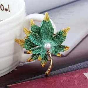 Gros plan détaillé sur l'élégante broche feuille d'érable vert-or avec une perle centrale.