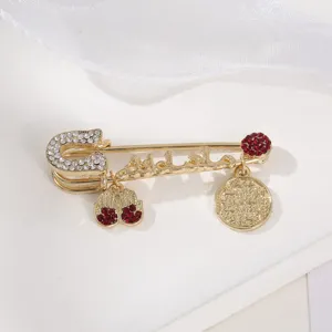 Elegant gold-tone safety pin brooch featuring sparkling rhinestones and chic dangling charms.
