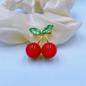 Close up shot of a cute cherry brooch with red beads and green crystal leaves on satin.