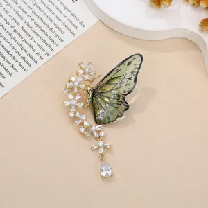 Dettaglio spilla a farfalla verde con strass scintillanti e un elegante ciondolo floreale raffinato.