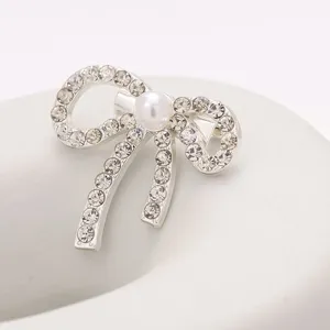 Broche nœud argentée avec strass et perle, vue de détail rapprochée de ce bijou élégant.
