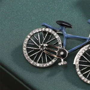 Close-up detail shot of a vintage bicycle brooch pin with sparkling rhinestones and blue enamel.