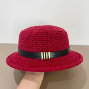 Red knit bucket hat detail showcasing retro black leather strap and chic vertical metal buckles.