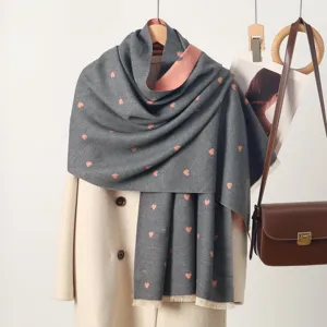 Close-up of a cozy grey winter scarf featuring cute pink heart prints and fringe details.