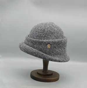 Vue detaillee du chapeau cloche en feutre de laine grise avec bord roule et ornementation metallique.