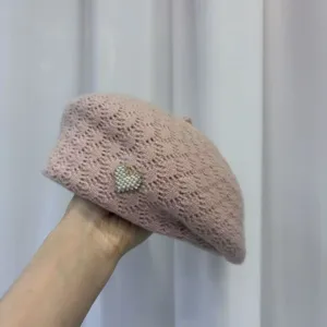 Close-up of pink knit pearl beret, soft woolen texture with cute heart charm detail.