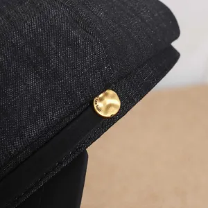 Gros plan détaillé sur le tissu en denim texturé et le bouton en métal doré de la casquette.