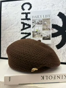Detailaufnahme der braunen Strickbarette, modischer Malerhut mit feinem goldenen Abzeichen.