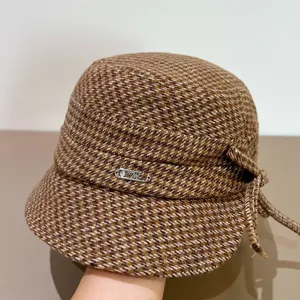 Nahaufnahme des braunen Tweed-Eimerhuts mit schicker Schleife und metallenem Logo-Pin.