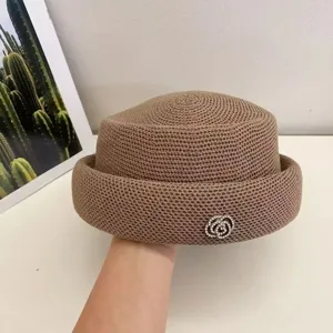 Vista dettagliata del cappello retrò in maglia marrone con spilla di camelie in strass.