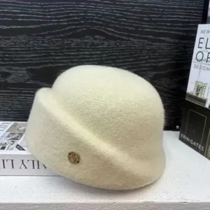 Detail shot of winter faux wool beret hat in cream white with gold metal logo accent.