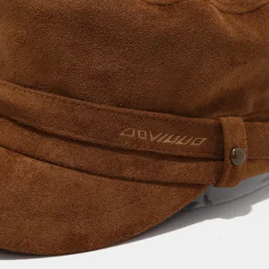 Close-up detail of brown suede military cap featuring custom embroidered logo and metal buckle.