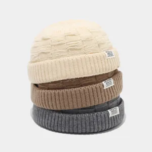 Gedetailleerd overzicht van drie gestapelde gebreide dockermutsen in beige, bruin en grijs label.