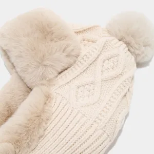 Dettaglio in primo piano del morbido cappello trapper in maglia beige con paraorecchie e pompon.