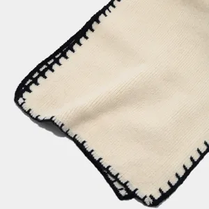 Detalle de bufanda de punto beige con borde de puntada de contraste negro, invierno cálido.