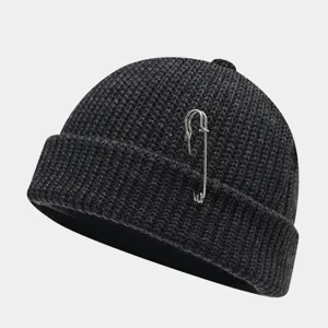 Close-up van donkergrijze gebreide muts met metalen veiligheidsspeld detail, streetwear stijl.