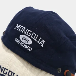 Detailopname van donkerblauwe canvas baret met witte borduursel en metalen knopen voor stijl.