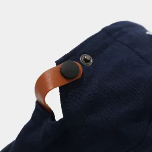 Detailopname van de donkerblauwe canvas pet met bruine lederen gesp en drukknop.