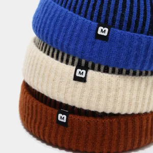 Detailaufnahme von gestapelten bunten Strickmützen mit Umschlag und kleinen M-Etiketten.