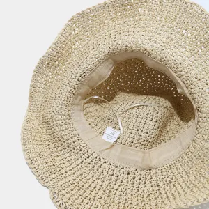 Gros plan sur l'intérieur du chapeau en paille tressée, montrant les détails de l'étiquette.